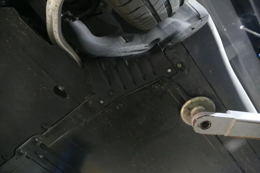 Close-up of the installed coolant hose guard plate on the Model Y underbody